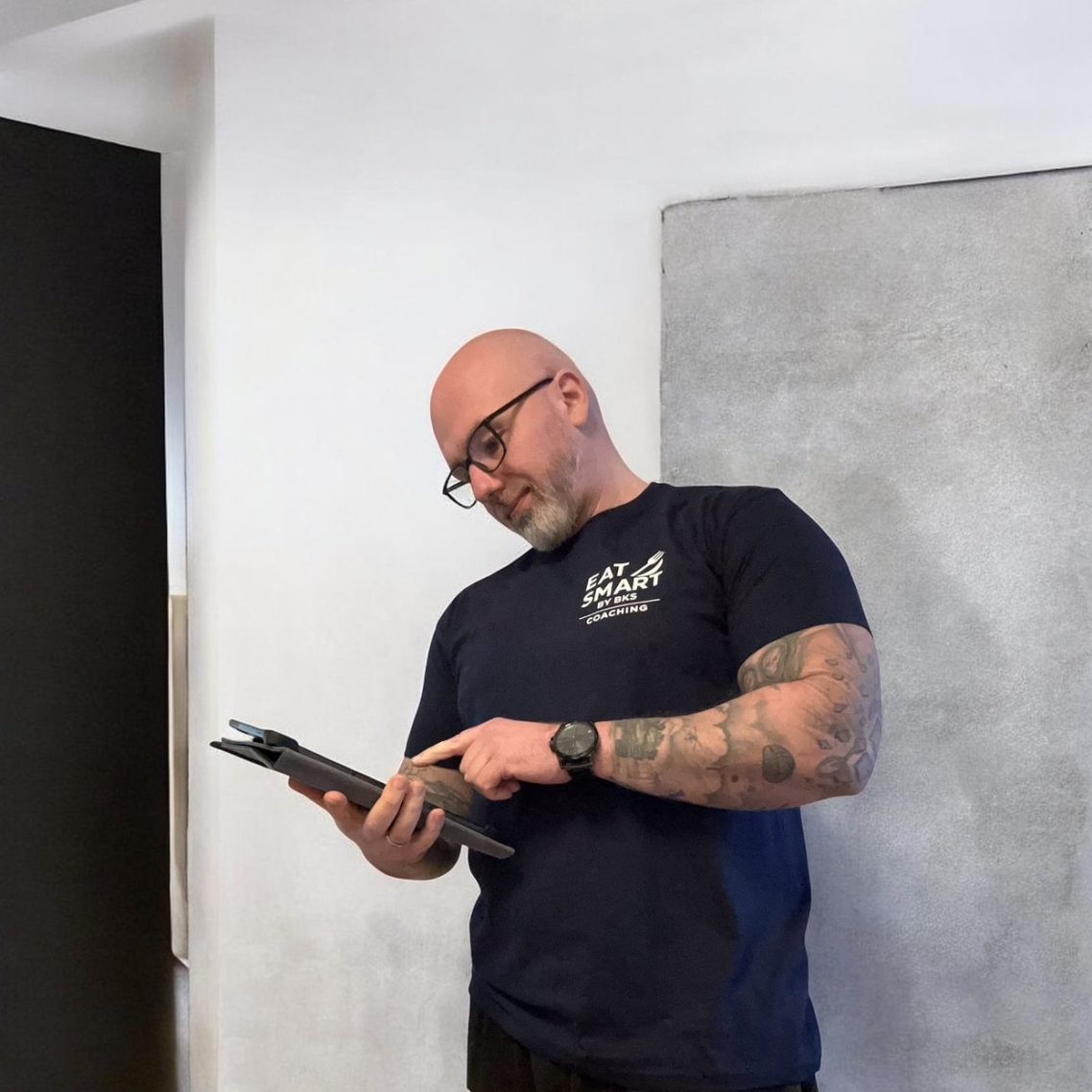 Online Coaching Lächelnder Mann in grauer Kapuzenjacke steht in einem modernen Fitnessstudio.